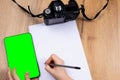 Flat lay, hands writing in a blank white page from digital mock up green screen tablet, decorated with vintage camera for Royalty Free Stock Photo