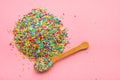 Flat lay of heap colorful sprinkles on wooden spoon over pink background, top view