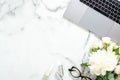 Flat lay home office desk. Female workspace with laptop computer, white flowers bouquet, accessories, cosmetic on marble