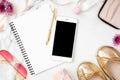 Flat lay home office desk. Female workspace with mobile phone, paper notepad, golden shoes and feminine accessories on marble Royalty Free Stock Photo