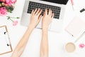 Flat lay home office desk. Woman workspace with female hands, laptop, pink roses bouquet, accessories, diary. Top view. Girl worki