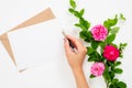 Flat lay home office desk. Women workspace with blank paper card, female hand holding pen, gift box, bouquet of rose flowers. Top Royalty Free Stock Photo