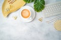 Flat lay home office feminine table with coffee cup, golden accessories, computer keyboard and tropical leaves on grey background