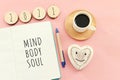 Flat lay image of notebook with words Mind, Body, Soul on pink wooden background