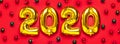 Flat lay 2020 inflatable golden numbers with red and green christmas balls on red background. New year winter decoration, holiday