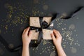 Flat lay of kids hands holding gift wrapped and decorated with bow on black background with copy space, stylish birthday,