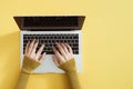 Flat lay of laptop, coffee and notebook on yellow background. Female hands typing on keyboard Royalty Free Stock Photo