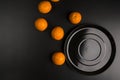 Flat lay of a large black plate and scattered oranges next to it. Dimmed lights. Space for text Royalty Free Stock Photo