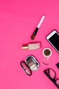 Flat lay of makeup products smartphone and women glasses on a rich pink paper background