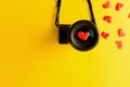 Flat lay of mirorless camera with lens and love red hearts on yellow background, engagement or couple wedding