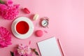 Flat lay with notepad, pencil, alarm clock, peony flowers, a cup of tea and macarons on a light pink background