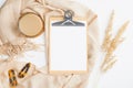 Flat lay paper clipboard, dry flowers, cup of coffee and beige blanket on white table. Cozy home office desk, modern feminine