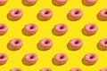 Flat lay pattern of tasty pink donut on yellow background