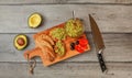 Flat lay photo, freshly prepared guacamole in small glass bowl, bread, tomatoes, olives at working board and two avocados next Royalty Free Stock Photo