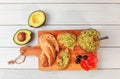 Flat lay photo, freshly prepared guacamole in small glass bowl, bread, tomatoes, olives at working board and two