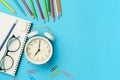 Flat lay photo of office desk with colorful pencil, Paper clip, Glasses, Note book, White retro clock, Top view of the copy space