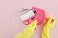 Flat lay photography female hands in yellow latex gloves with brush and dustpan clean the dirt on pink background. Copy