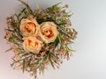 Flat lay photography of 3 peach rose flower blooms surrounded by a pink and green wreath on a white background. Simple home decor