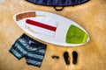 Flat lay photography of a white skimboard with red, white and green pads, with some orange surf wax on the nose in the middle of