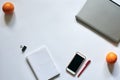 Flat-lay picture of office accessories, isolated on white background. Grey laptop, white smart phone, red pen, notepad and oranges Royalty Free Stock Photo