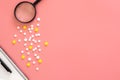 Flat lay, pills and magnifier on pink background, copy space.