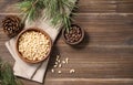 Flat lay of pine nuts in a bowl on napkin and a handful of unpeeled nuts on a brown wooden background with a branch of pine