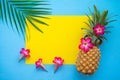 Flat lay of pineapple, flowers, palm leaf on yellow and blue background with copy space, tropical summer holiday Royalty Free Stock Photo
