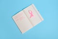 Flat lay of a pink ribbon, on opened notepad with inscriptions reminding of a medical check-up. October 1st, World Breast Cancer