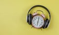 Flat lay of pink vintage alarm clock show 6 o`clock cover with headphones on yellow background ,time to listen to music concept