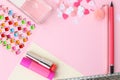 Flat lay: pink and yellow paper and pencil. Pink pen with pompom. Perfume with lipstick, hearts, glue,ruler and rhinestones