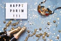 Flat lay of Purim Carnival celebration concept. Happy Purim written in light box, champagne bottles and carnival mask on blue