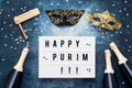 Flat lay of Purim Carnival celebration concept. Happy Purim written in light box, champagne bottles, carnival mask and wooden