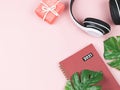 Flat lay of red 2021 diary or planner, headphones , red gift box and monstera leaves on pink background with copy space. Audio