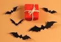 Flat lay of red gift box with black paper bats on orange background with copy space. Halloween present concept