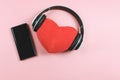 Flat lay of red heart pillow coverd with headphones and blank black screen mobile phone on pink background. Love songs or podcast Royalty Free Stock Photo