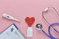 Flat lay of red heart shape of medicine pills and doctor equipment on pink background.