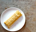 Top down view of sausage roll on a white plate on a brown background