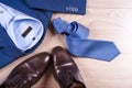 Flat lay set of classic mens clothes such as blue suit, shirts, brown shoes, belt and tie on wooden background.