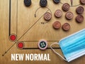 Flat lay shot a image word - NEW NORMAL and face mask/striker/carrom mens ball on carrom board with selective focus.