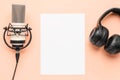 Flat lay shot of professional headphones and a radio microphone with a blank sheet of paper in the center, on a light peach