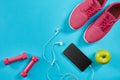 Flat lay shot of Sport equipment. Sneakers, dumbbells, earphones and phone on blue background.