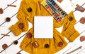 Flat lay of sketchbook, paints with brushes, yellow sweater, leaves, cinnamon sticks and pine cones on a white wooden background. Royalty Free Stock Photo