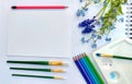 Flat lay sketchbook and pink violet, blue, purple and green pencils on white background. Royalty Free Stock Photo