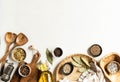 Flat lay of small bowls various dry spices, wood kitchen utensils and olive oil in glass bottle on light background. Top view.