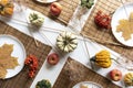 small pumpkins and dry brown maple leafs on white plates, autumn dinner table