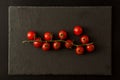 Flat lay. Sprig of cherry tomatoes on a black cutting board. Black background