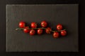 Flat lay. Sprig of ten cherry tomatoes on a black cutting board. Black background