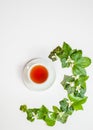 Vertical flat-lay pattern with ivy leaves and white spring flowers together with a cup of tea. White background. Copy space. Royalty Free Stock Photo