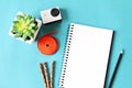 Flat lay style of office workspace desk with blank notebook paper, small action camera and accessories on blue background