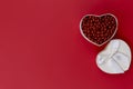 FLAT LAY STYLE. On a red paper surface on the right is a white heart-shaped box with red beads. Royalty Free Stock Photo